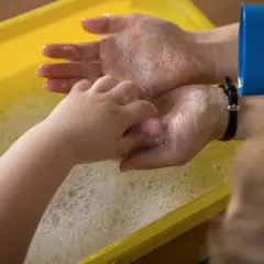 Dziecko i dorosły myją ręce w żółtej wannie z pianą.